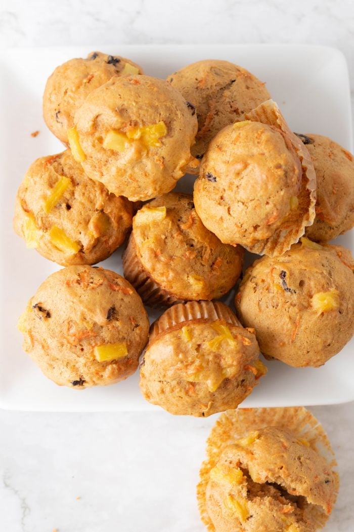 top down view of carrot pineapple muffins piled on a plate, one broken one is laying on the table